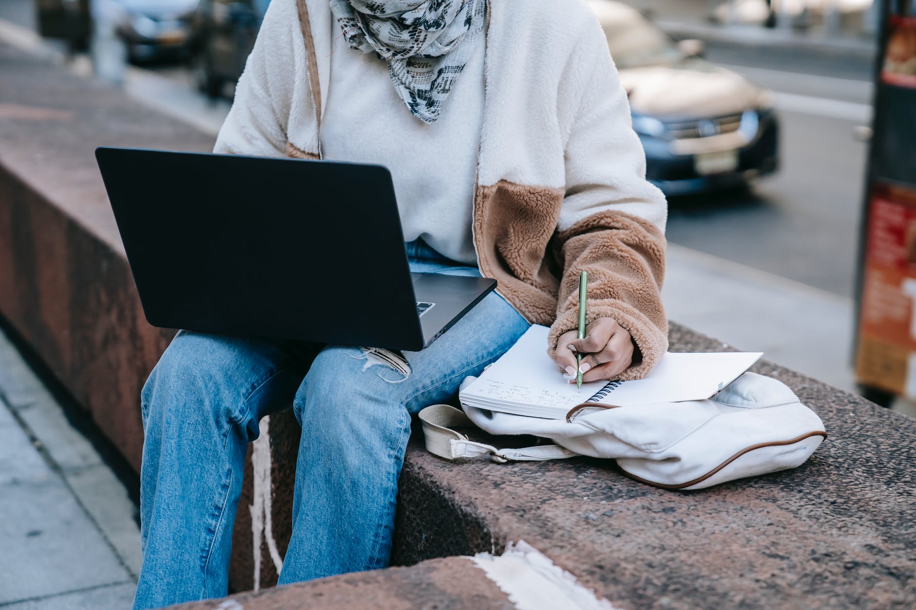 anonymous female using laptop and taking notes on street